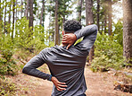 Man holding his neck and back in pain while out for a run in the woods. Fit man experiencing discomfort in his body while exercising in a nature environment 