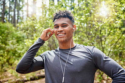 One active young man listening to music with earphones while exercising at the park. Confident mixed race athlete staying motivated with songs from playlist for a run or jog in the morning outside