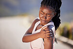 Active young black woman holding her shoulder in pain while exercising outdoors. Athlete suffering with a sore arm injury, causing discomfort and strain. Bone and muscle sprain from a fractured joint