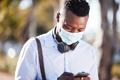 Buy stock photo Unrecognizable black man wearing a mask to protect himself from the corona virus pandemic while wearing earphones and texting on a cellphone. Businessman walking to a an interview using gps on a phone