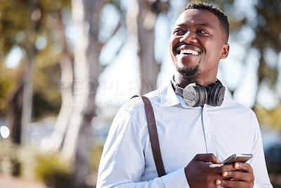 Happy african american businessman wearing headphones and texting on a cellphone while commuting in the city. One young black guy looking thoughtful while using apps and browsing social media online
