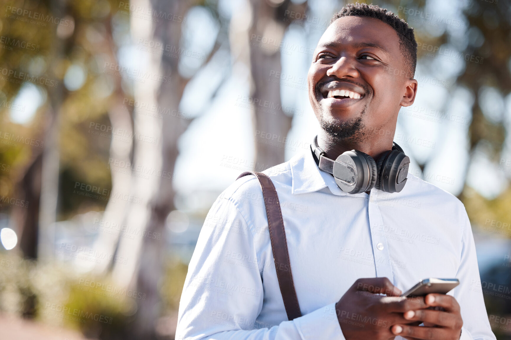 Buy stock photo Happy african american businessman wearing headphones and texting on a cellphone while commuting in the city. One young black guy looking thoughtful while using apps and browsing social media online