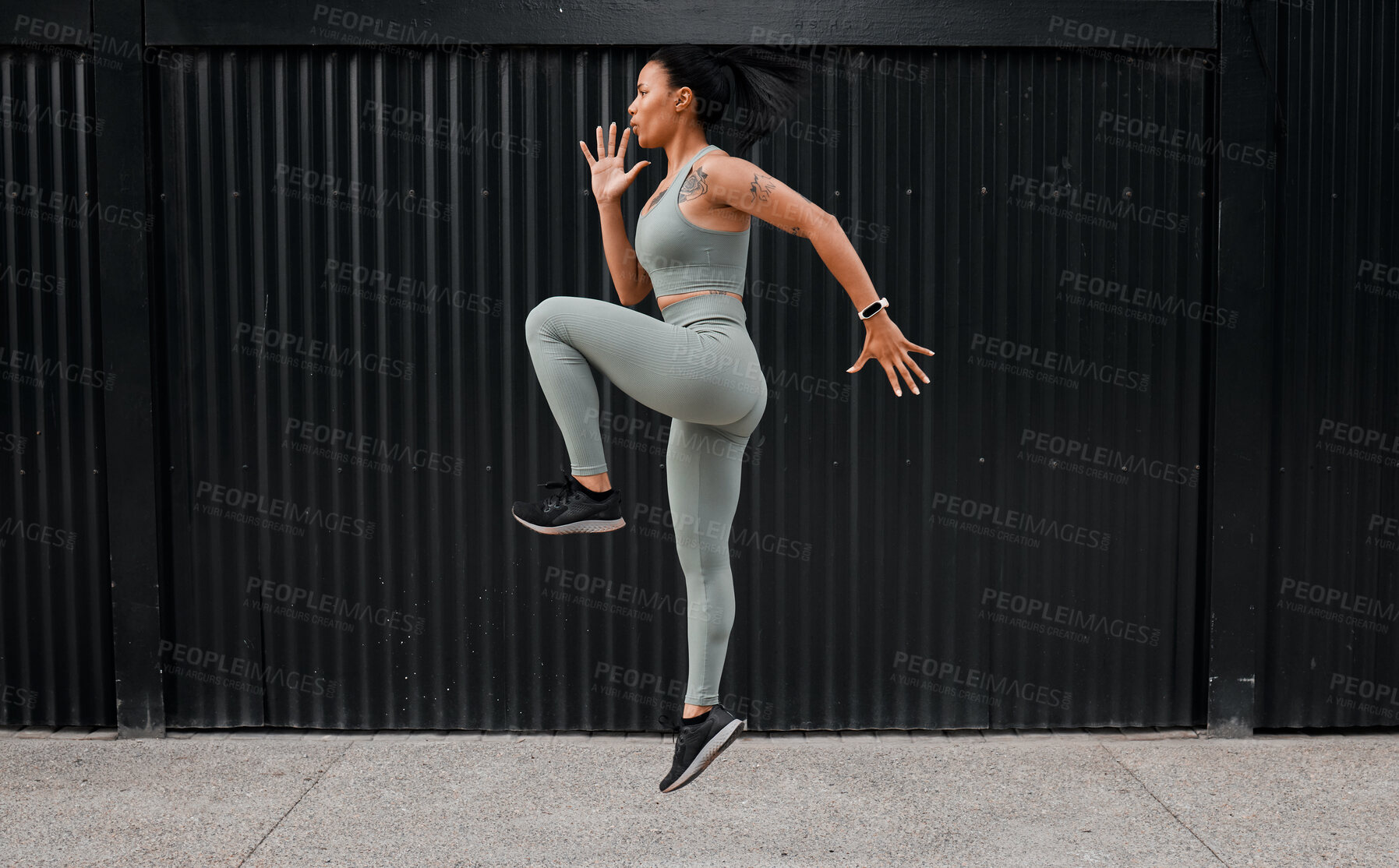 Buy stock photo One young african american female athlete running on the spot while exercising outside in the city. Beautiful and dedicated mixed race sportswoman working out alone against an urban background