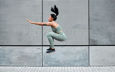 One sporty young african american woman jumping while exercising outside. A beautiful brunette mixed race female athlete working out in the city. Dedicated to fitness and living a healthy lifestyle