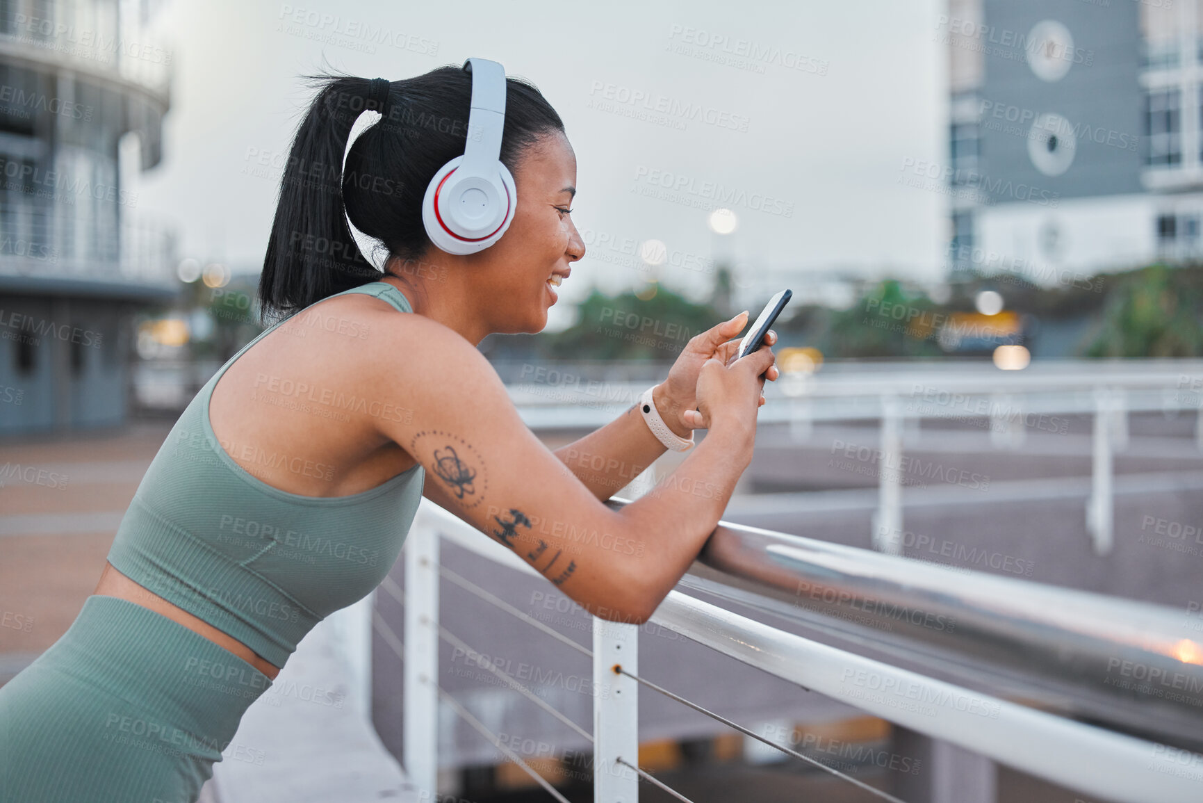 Buy stock photo Sporty young african american woman texting while exercising outside. Mixed race female athlete using a cellphone in the city. Checking social media while taking a break to enjoy music with headphones