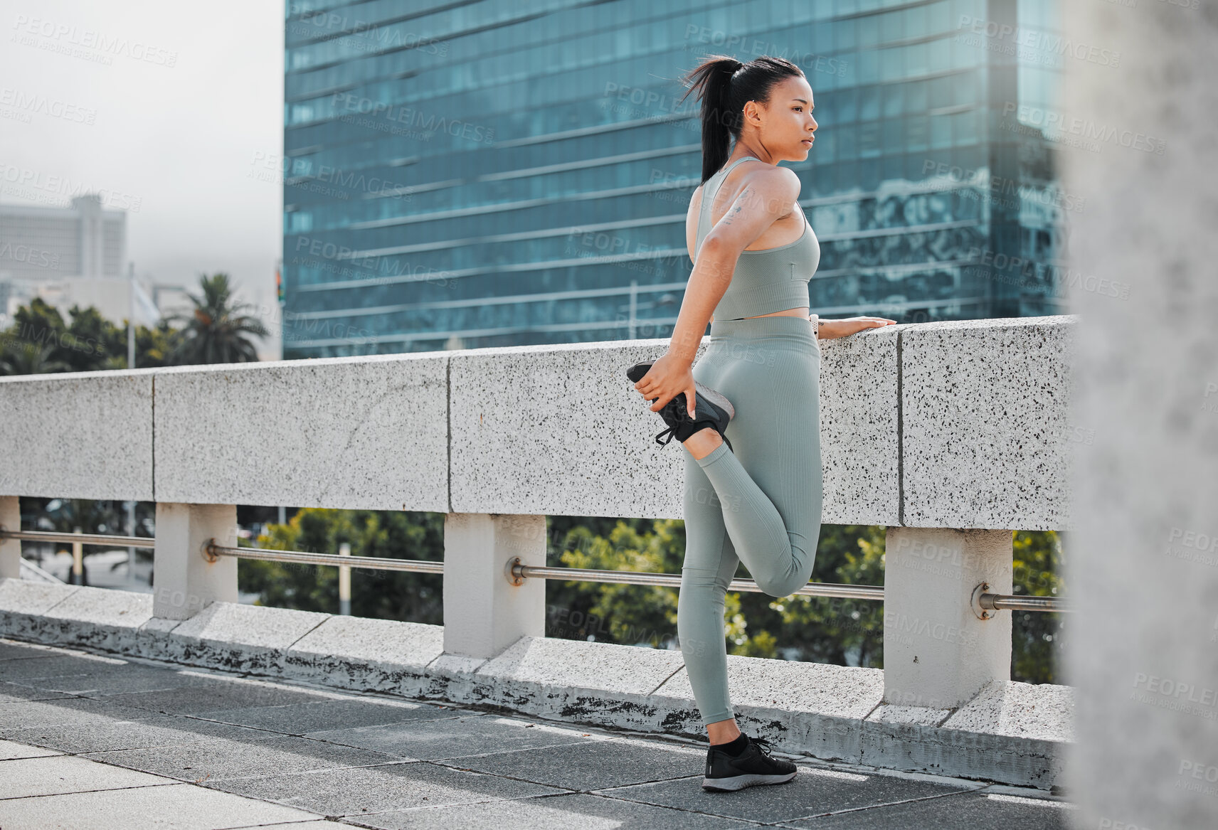 Buy stock photo One fit young woman wearing workout clothes and stretching her legs while standing on a bridge and looking at the view in the city. Hispanic athlete focused on health and wellness and getting ready for a workout downtown