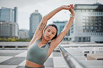 Portrait of a young mixed race female athlete looking serious while stretching her arms before her run in the city. Young woman warming up her muscles while during exercise against a urban background