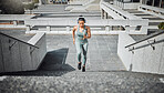 Young mixed race female athlete wearing gymwear and headphones while running up the steps of a building outside. Young female focused on her speed, body, fitness and cardio health while training