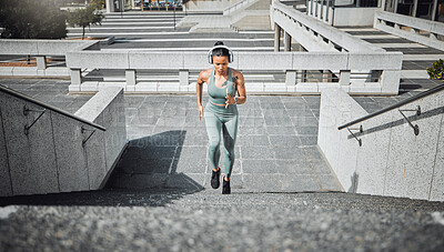 Buy stock photo Young mixed race female athlete wearing gymwear and headphones while running up the steps of a building outside. Young female focused on her speed, body, fitness and cardio health while training