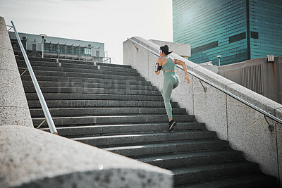 Rear view of a female wearing athlete wearing a phone armband and headphones while running up the steps of a building outside. Young female focused on her speed, body, fitness and cardio health while training