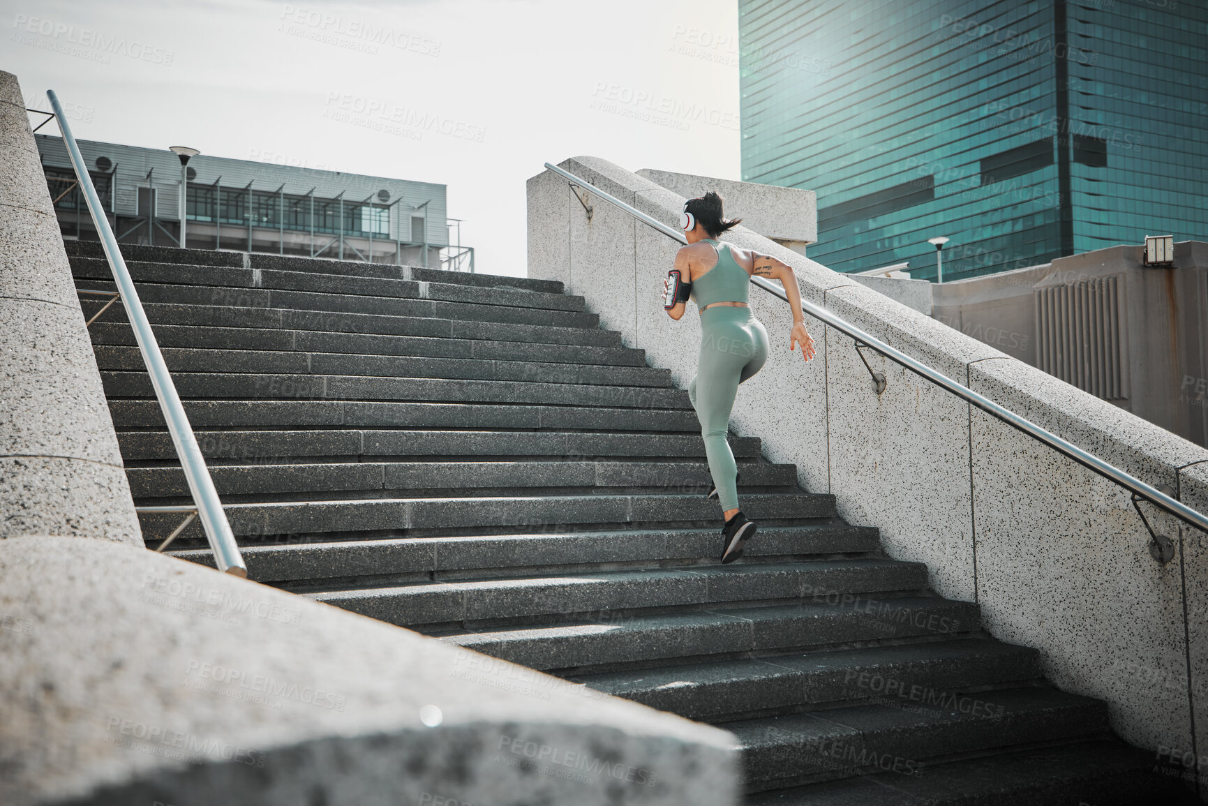 Buy stock photo Rear view of a female wearing athlete wearing a phone armband and headphones while running up the steps of a building outside. Young female focused on her speed, body, fitness and cardio health while training