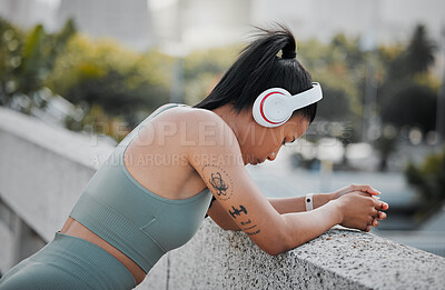 Buy stock photo Young mixed race sportswoman wearing headphones listening to music and taking a break from running outside in the city. Exercise is good for your health and wellbeing