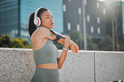 Buy stock photo Young fitness woman wearing headphones and listening to music while stretching before a run outside in the city. Exercise is good for health and wellbeing
