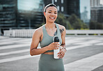 Happy young mixed race fit female athlete smiling while taking a break holding water bottle and working out in the city. Exercise is good for your health and wellbeing