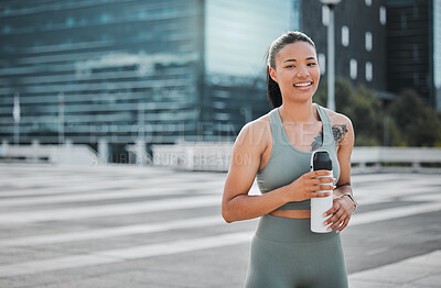 Young mixed race fit female athlete smiling and looking happy while taking a break resting drinking water and working out outside in the city. Exercise is good for your health and wellbeing