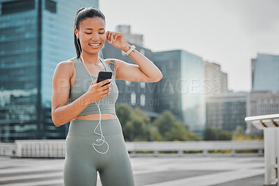A young female athlete looking happy and smiling while wearing earphones and listening to music from a cellphone and reading a text message in the city. Woman enjoying a break from exercising outside.