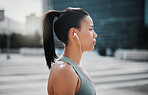Profile view of a young serious looking mixed race female athlete wearing earphones and listening to music while standing outside in the city. Determined, focused, workout. Taking a break