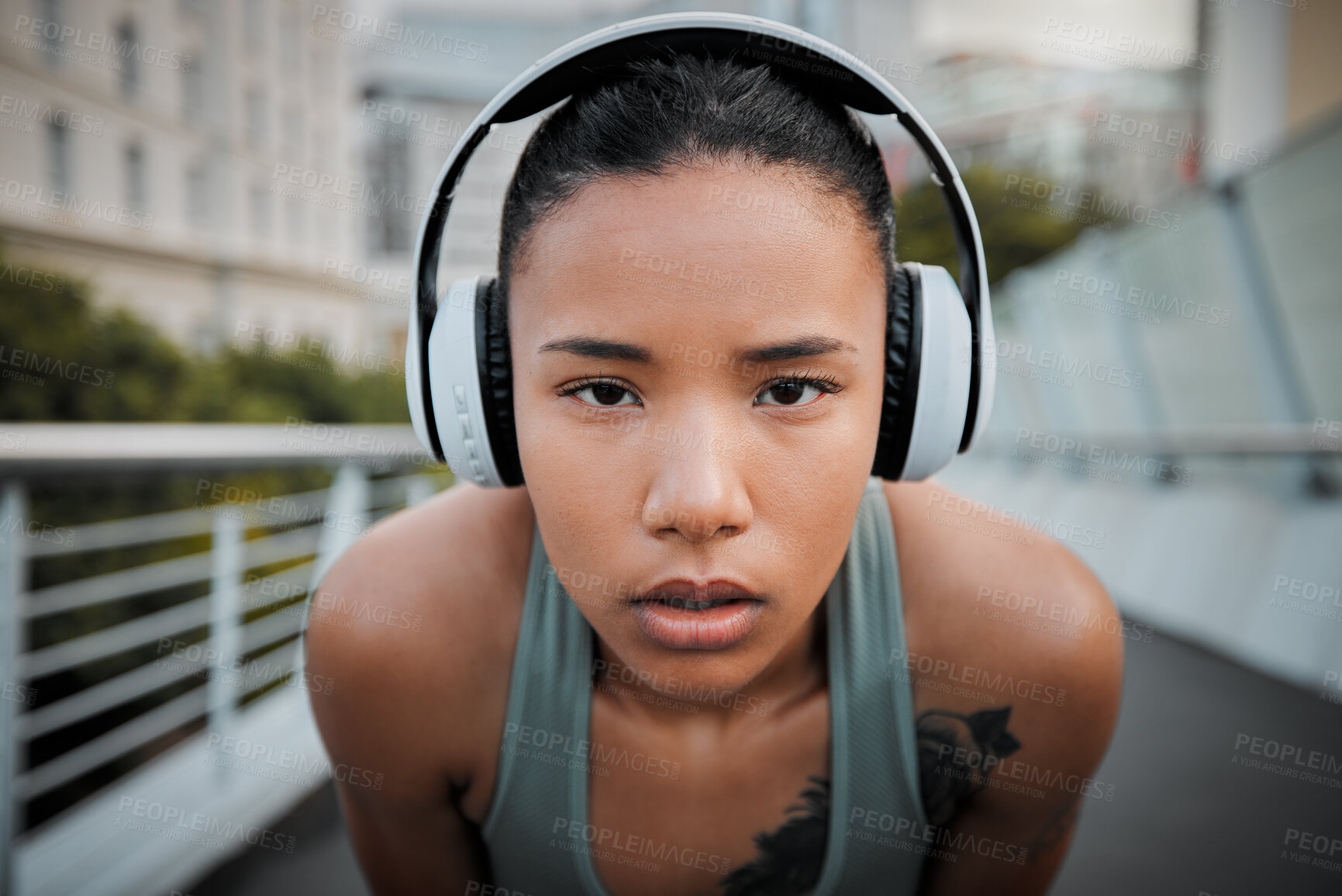 Buy stock photo Close up portrait of a young mixed race female athlete wearing wireless headphones and listening to music while standing outside in the city. Determined to get fit and focused on health