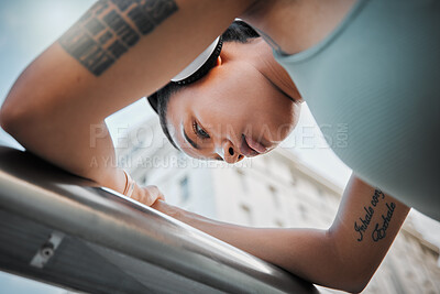 Buy stock photo Below shot of a beautiful young mixed race sportswoman listening to music while working out in the city. Young female athlete looking tired and resting while using wireless headphones outdoors