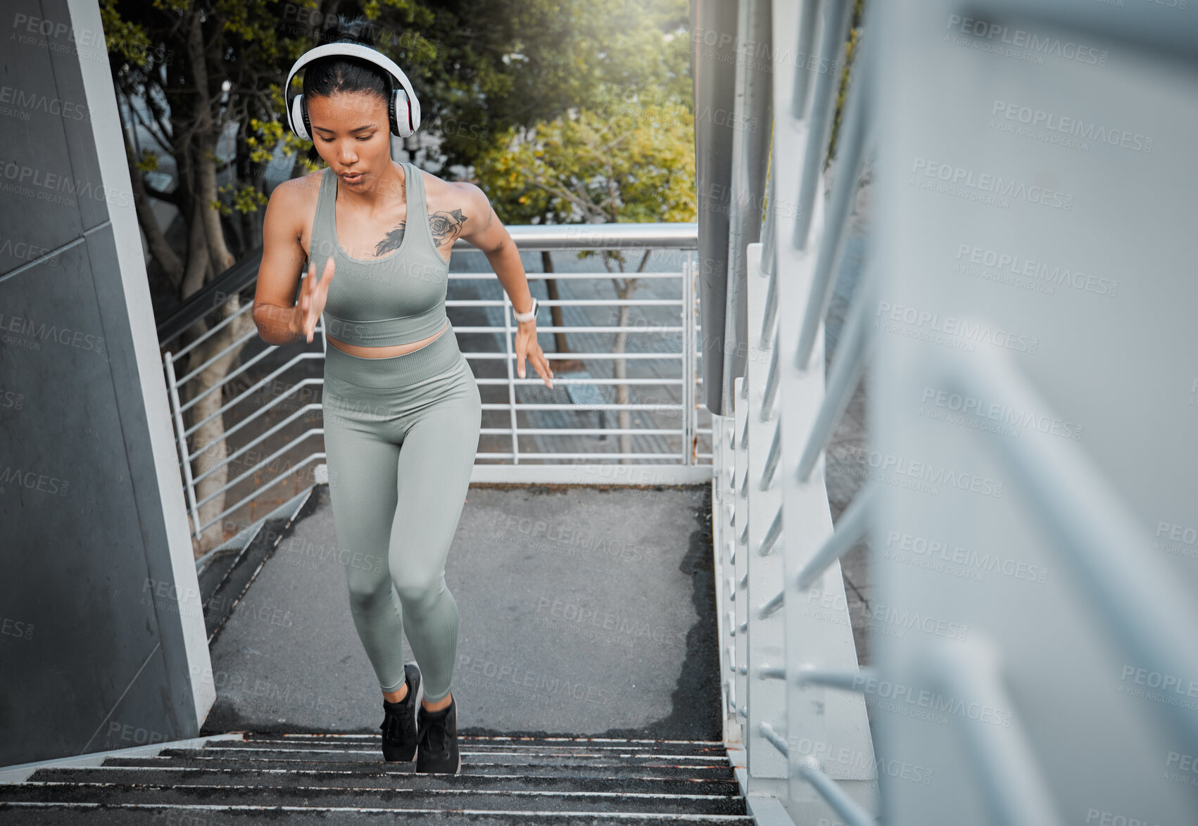 Buy stock photo Young fit athletic mixed race woman running up stairs during outdoor workout in city while listening to music through headphones. Hispanic woman focused on health, physical activity, strength, cardio