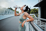 Young mixed race female athlete taking a break resting and drinking water from a bottle while working out outside in the city. Exercise is good for your health and wellbeing
