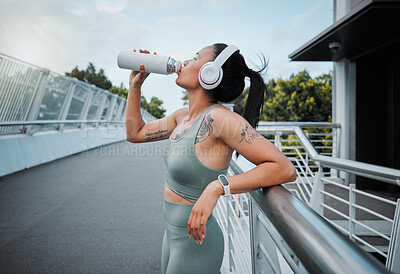 Young mixed race female athlete taking a break resting and drinking water from a bottle while working out outside in the city. Exercise is good for your health and wellbeing