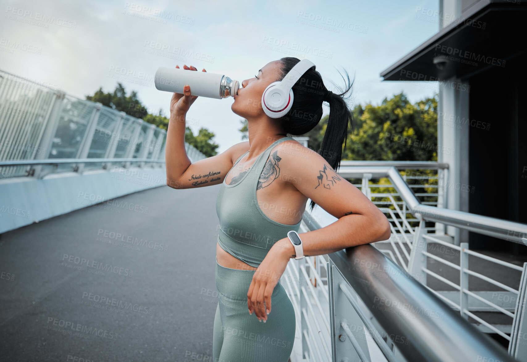Buy stock photo Young mixed race female athlete taking a break resting and drinking water from a bottle while working out outside in the city. Exercise is good for your health and wellbeing