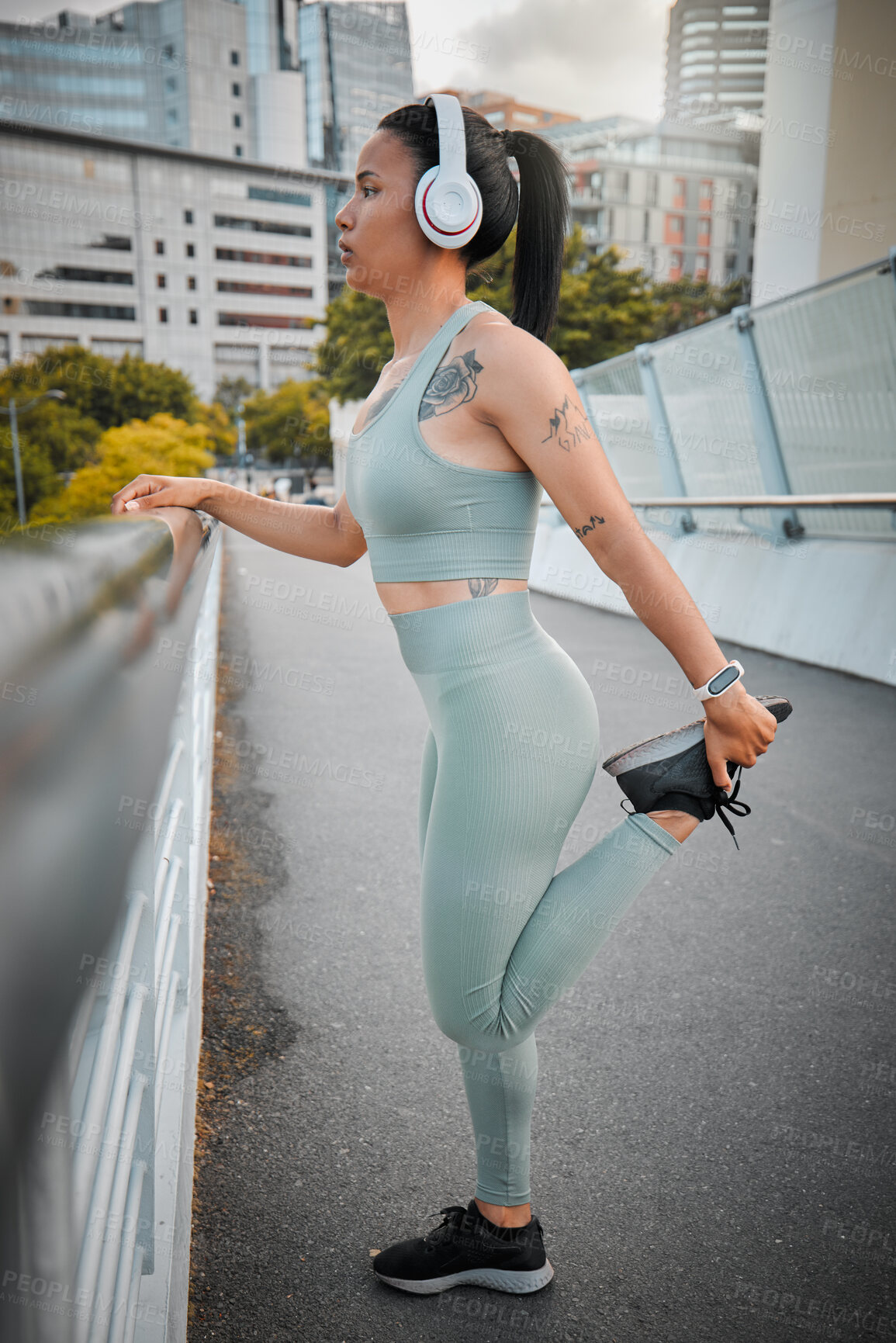 Buy stock photo One young fit and active mixed race woman standing alone and stretching before exercising in a city. Hispanic athlete focused on health and wellness, warming up and listening to music on headphones while out for a run