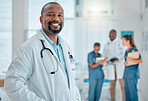 Happy mature african american male doctor standing while working at a hospital with colleagues. Expert medical professional smiling while at work at a clinic with coworkers