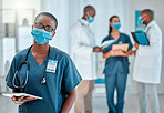 Portrait of a young african american female doctor working on a digital tablet and wearing a mask while working at a hospital with colleagues. Black female nurse doing research on a digital tablet at work at a clinic