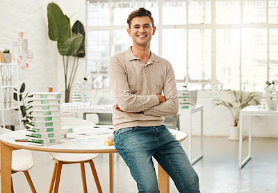 Portrait of a confident young businessman in his office. Young designer with his arms crossed. Architect sitting on his desk in an agency. Creative small business owner in his office.