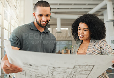 Young coworkers looking at a blueprint. Two businesspeople collaborate on a building plan. Design creatives working together in a modern office. Happy colleagues plan a building project together