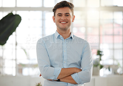 Buy stock photo Young caucasian businessman standing with his arms crossed in an office alone at work. One happy male businessperson smiling while standing at work