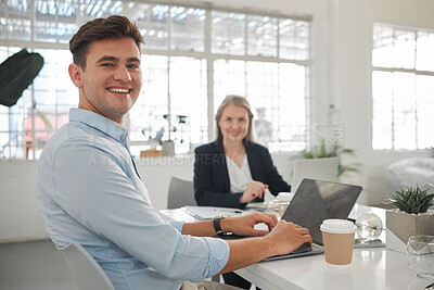 Buy stock photo Portrait of a young caucasian businessman working on a laptop with a colleague at work. Happy male businessperson typing en email on a laptop in an office