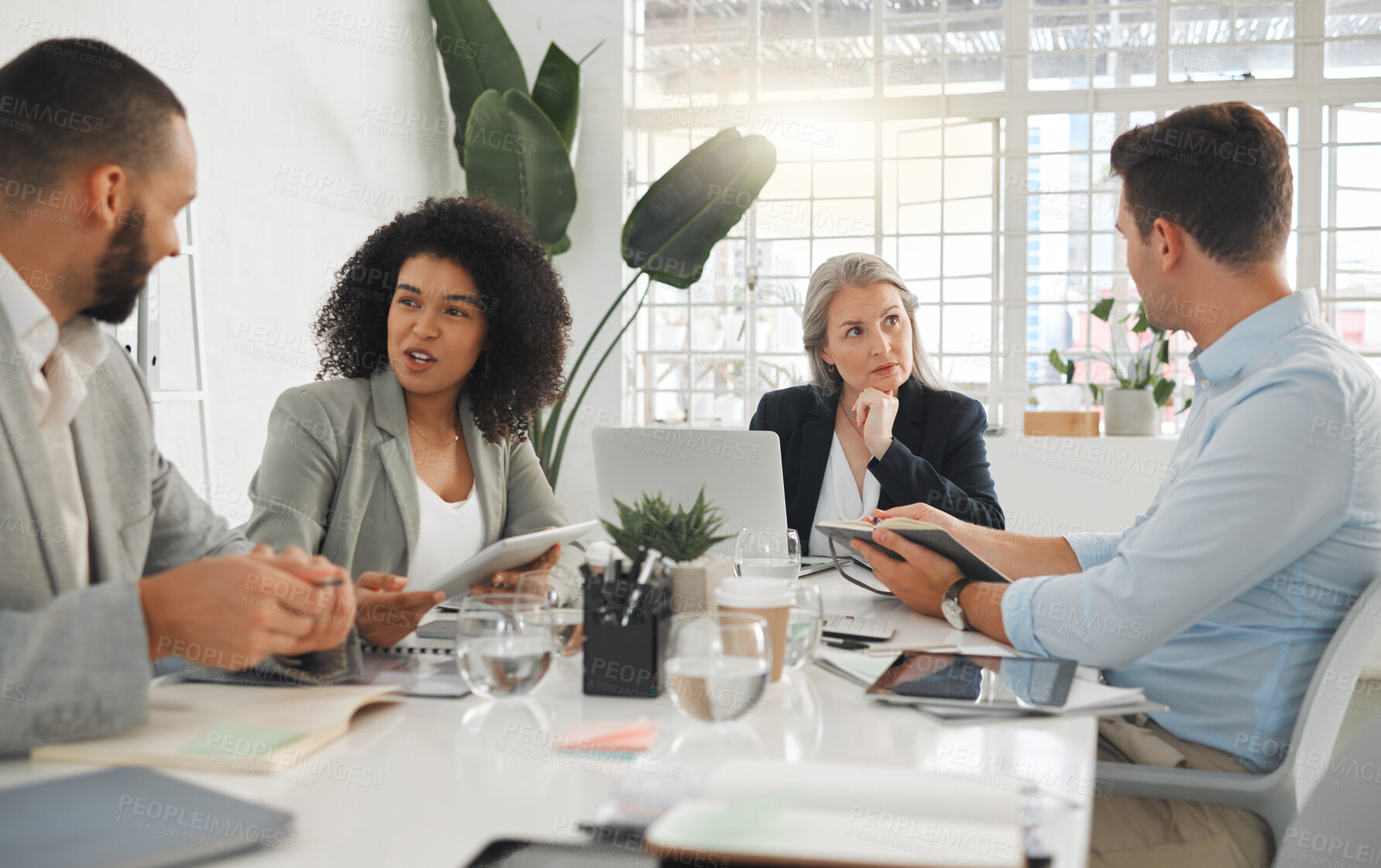 Buy stock photo Diverse group of businesspeople having a meeting together at a table at work. Business professionals talking and planning while using technology in an office. Male and female coworkers discussing a business strategy