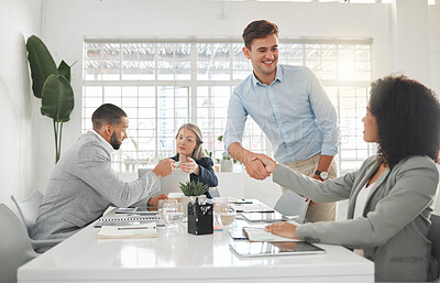 Buy stock photo Diverse group of businesspeople having a meeting together at a table at work. Business professionals talking and planning in an office. Young caucasian businessman greeting a mixed race businesswoman with a handshake