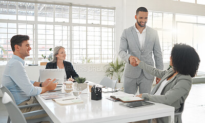 Buy stock photo Diverse group of businesspeople having a meeting together at a table at work. Business professionals talking and planning while using technology in an office. Hispanic businessman greeting a mixed race businesswoman with a handshake