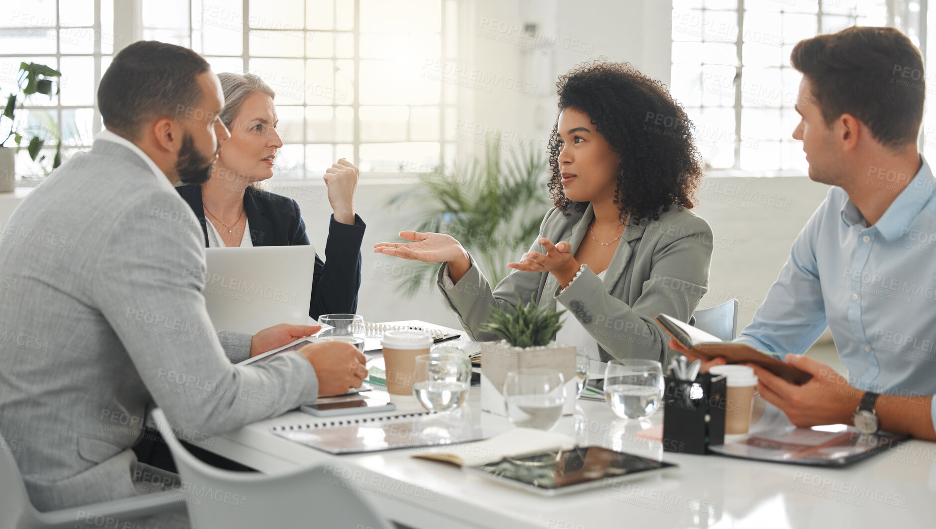 Buy stock photo Young mixed race businesswoman with a curly afro explaining an idea in a meeting at work. Group of businesspeople having a meeting together at a table. Business professionals talking and planning in an office
