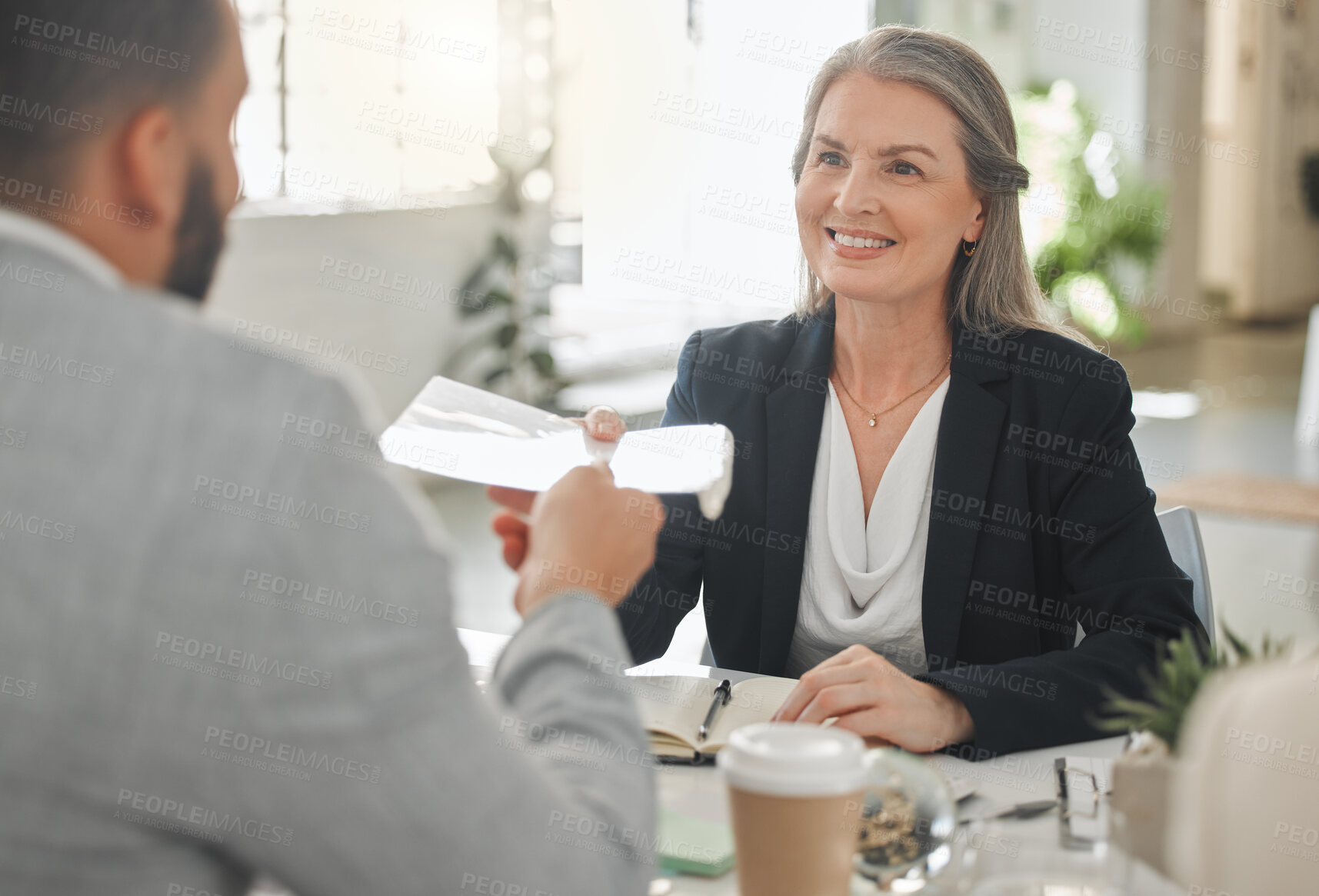 Buy stock photo Young happy mixed race businessman giving a report to a female caucasian colleague while in a meeting together at work. Mature businesswoman taking a document from an hispanic male coworker