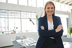 Mature happy caucasian businesswoman standing with her arms crossed while in an office alone. One confident and content female boss smiling and standing at work