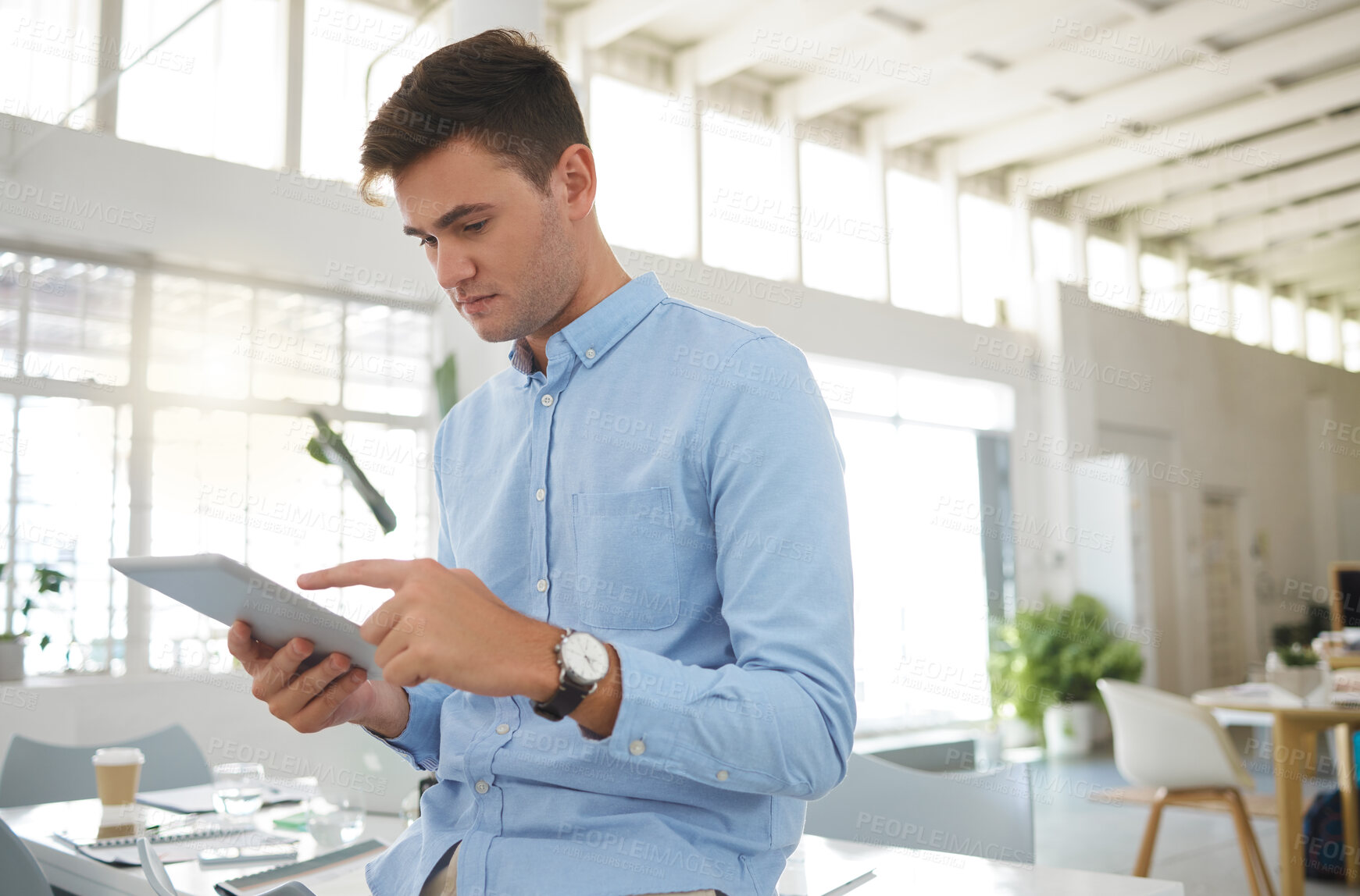 Buy stock photo Young caucasian businessman working on a digital tablet alone in an office. One male boss holding and using social media on a digital tablet at work