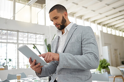 Buy stock photo Young focused mixed race businessman working on a digital tablet in an office. One hispanic male boss holding using social media on a digital tablet at work