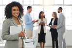 Young happy mixed race businesswoman standing in an office. One confident hispanic female boss with a curly afro smiling and standing while in a meeting at work