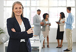 Mature caucasian businesswoman standing with her arms crossed while in an office with colleagues. Happy female boss In a meeting with coworkers