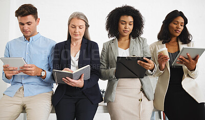 Buy stock photo Group of serious diverse businesspeople standing and using digital tablets and writing in notebooks together in an office. Content business professionals working and planning at work