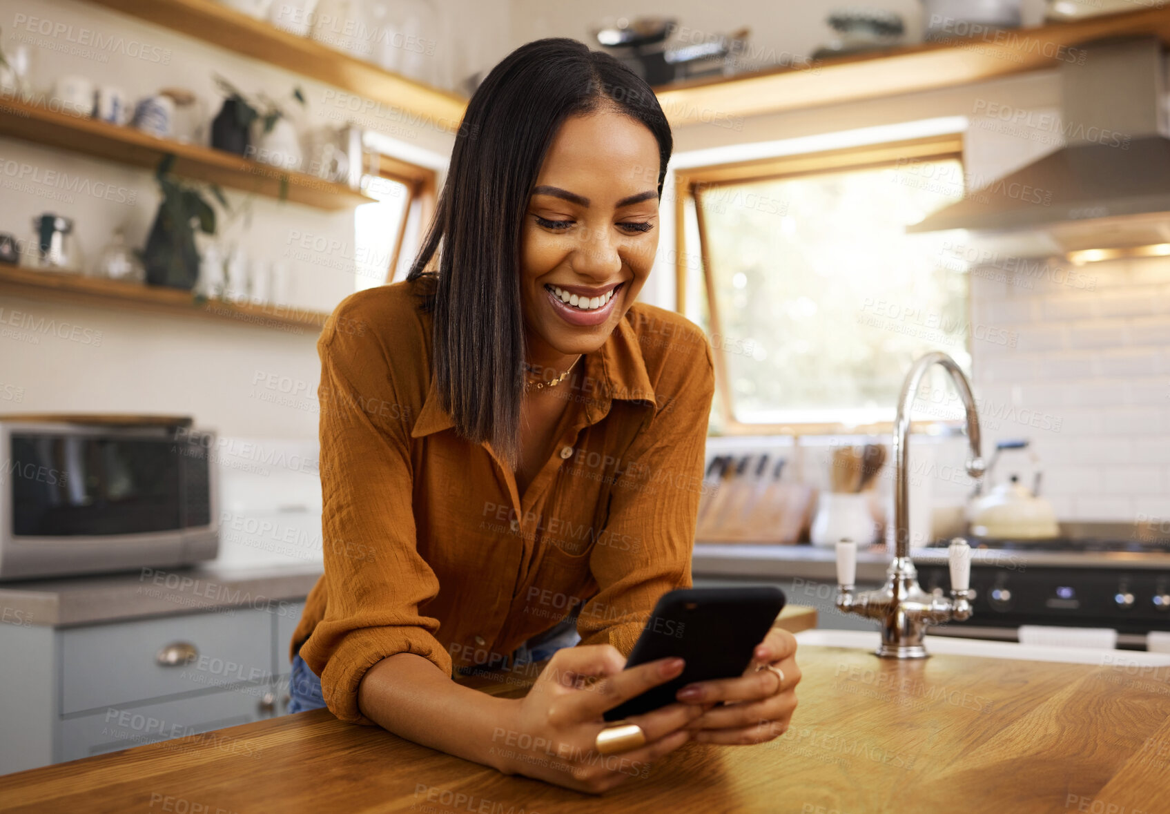 Buy stock photo Happy woman, phone text and kitchen in a home reading a web app. House, female and smile of a young person with joy resting on a counter top table feeling relax typing with mobile networking