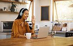 Young happy mixed race businesswoman waving while on a virtual meeting using a laptop at home. One hispanic female businessperson talking and greeting wearing headphones while on a call using a laptop