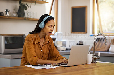 Young mixed race businesswoman going through paper and bills while working on a laptop at home. One hispanic female businessperson using a laptop and listening to music while working from home