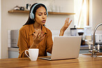 Young serious mixed race businesswoman talking while on a virtual meeting using a laptop at home. One hispanic female businessperson talking and wearing headphones while on a call using a laptop