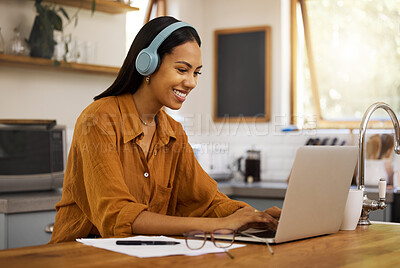 Young cheerful mixed race businesswoman going through paper and bills while working on a laptop at home. One happy hispanic female businessperson using a laptop and listening to music while working from home